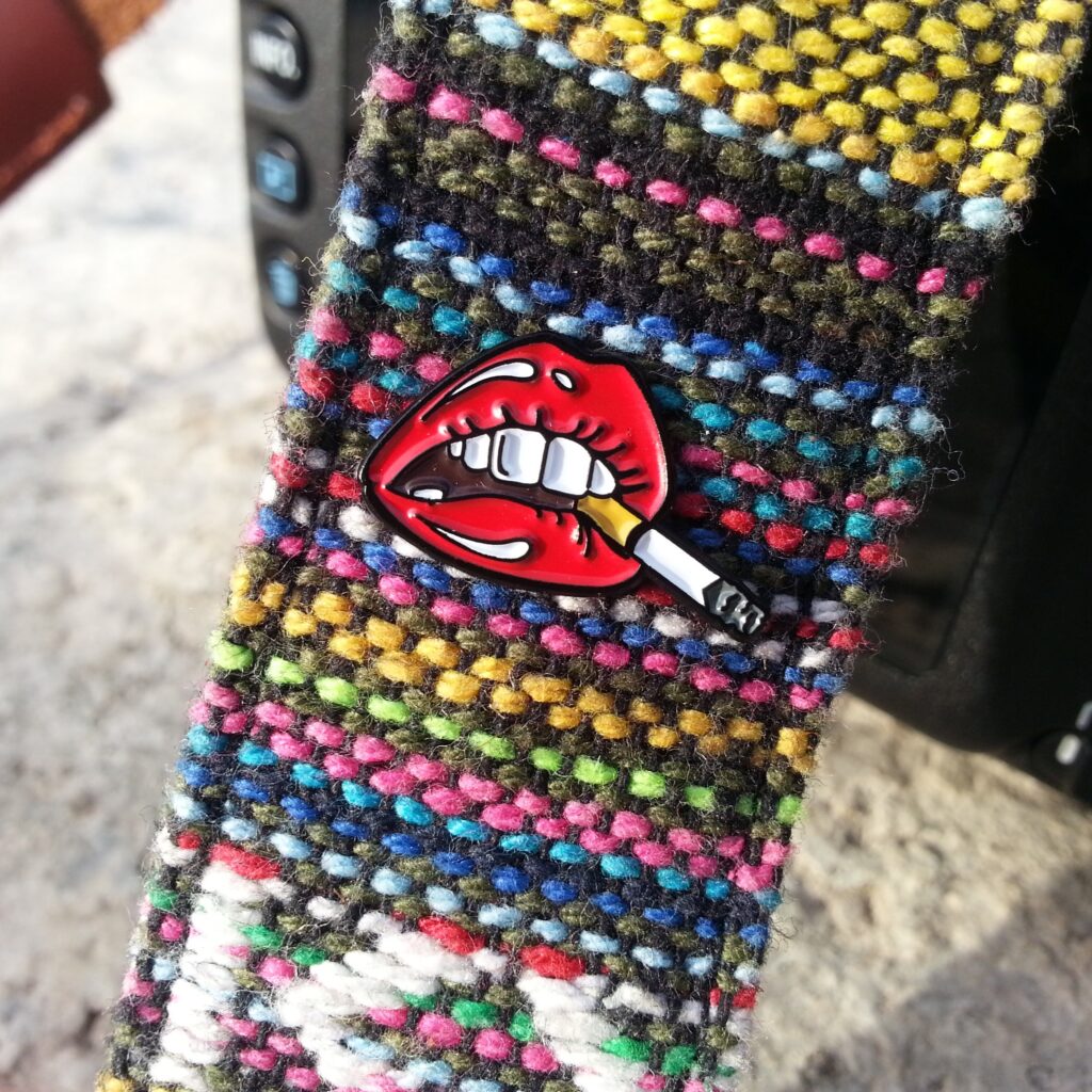 photo of a lapel pin in the shape of lips smoking a cigarette, clipped onto a camera strap