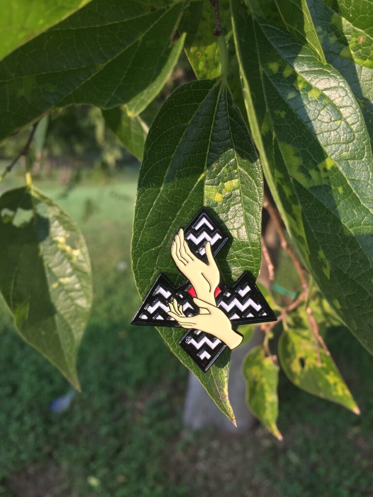 twin peaks lapel pin - laura palmer hands on top of twin peaks symbol with black and white zig zags