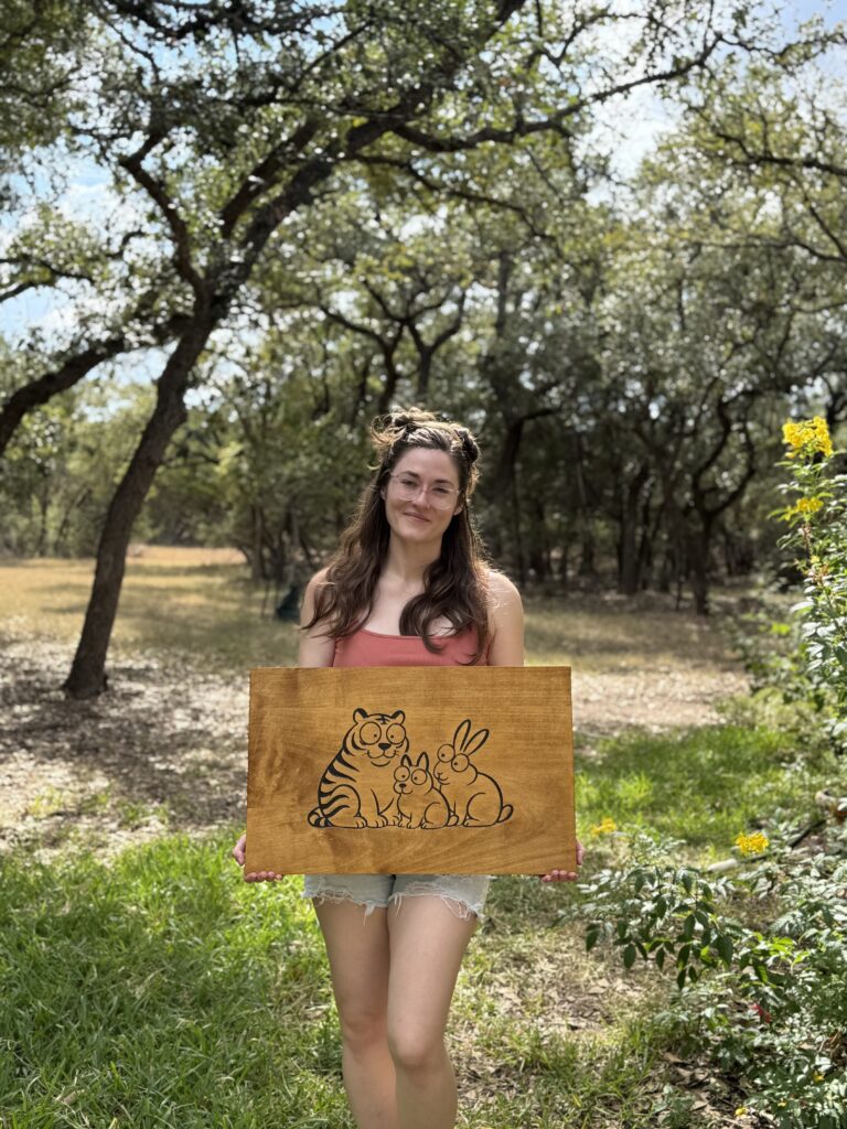 woman holding a wood sign with cartoon animals carved and painted into the face
