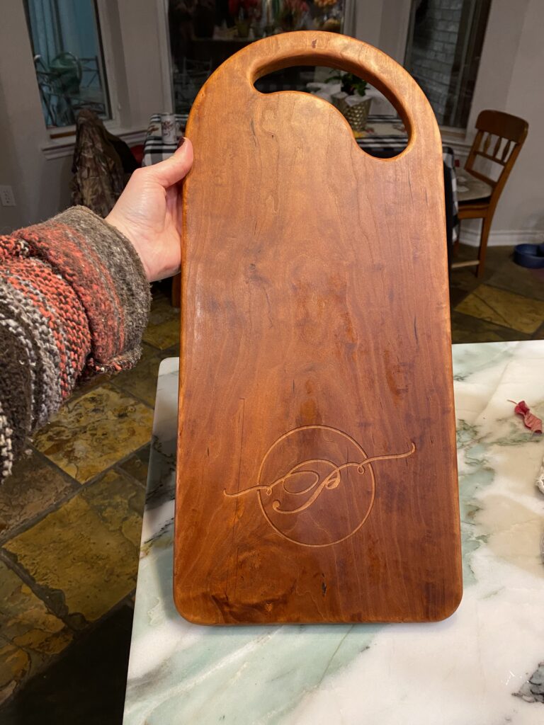 hand holding up a charcuterie board with rounded top and handle, with rounded bottom corners with a cursive P